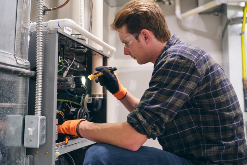 A repairman working inside a home, repairing a furnace.